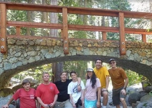 A group of volunteers standing on creek boulders beneath a stone arch bridge