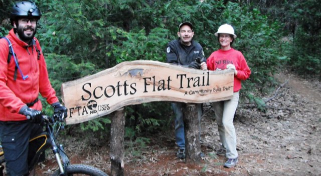 Volunteers and a mountain biker beside a carved wooden Scotts Flat Trail sign