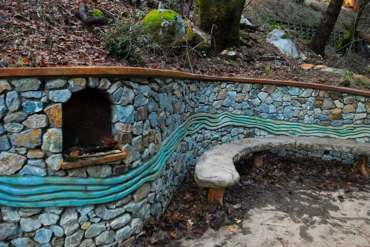 Hand-laid stone retaining wall with a turquoise wave inlay and a curved bench beside the trail