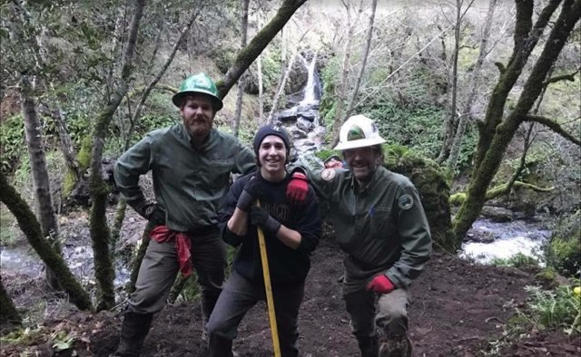Three trail workers in hard hats posing on fresh tread in front of a waterfall